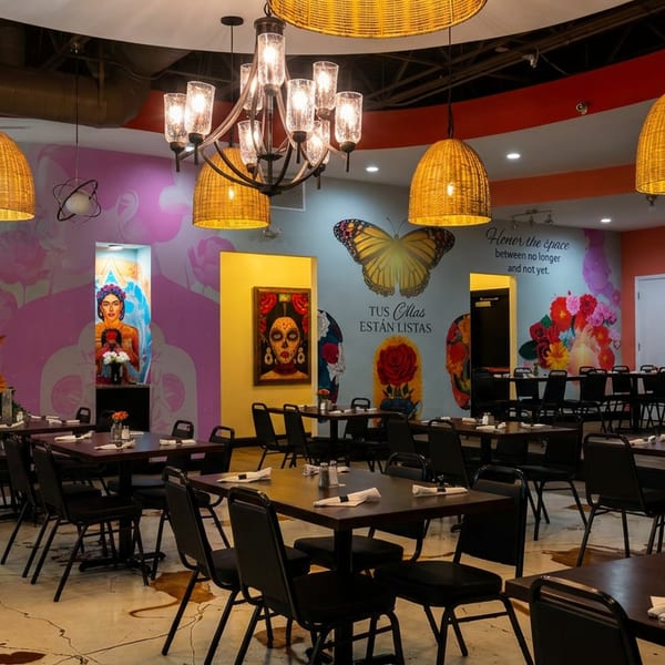 Vibrant, colorful dining room with murals, dark tables, and chairs, illuminated by wicker pendant lights.